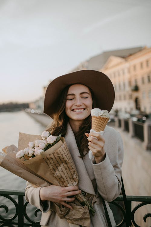 Free Woman Wearing Brown Coat Holding White Flower Bouquet And Ice Cream Stock Photo