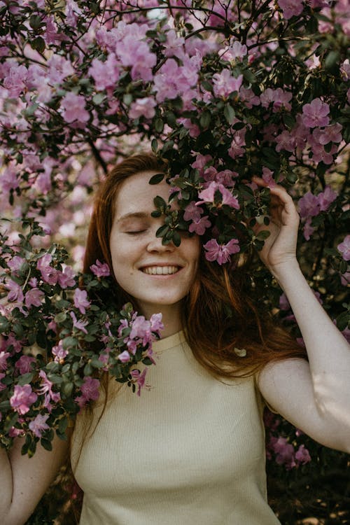 Foto De Uma Mulher Sorridente Posando Sob Uma Planta Com Flores Rosa Com Os Olhos Fechados