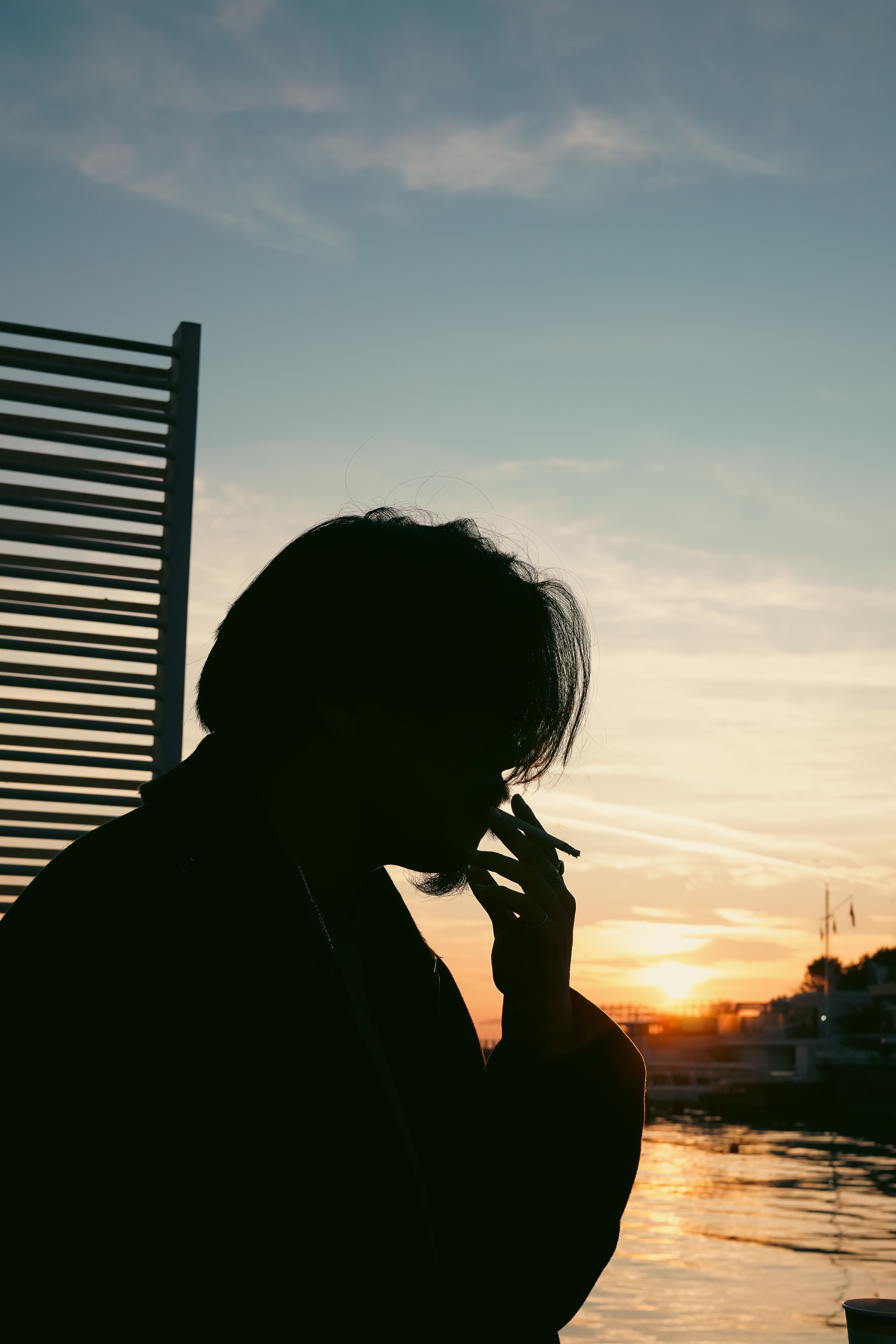 Silhouette of Person Smoking at Sunset by Water · Free Stock Photo