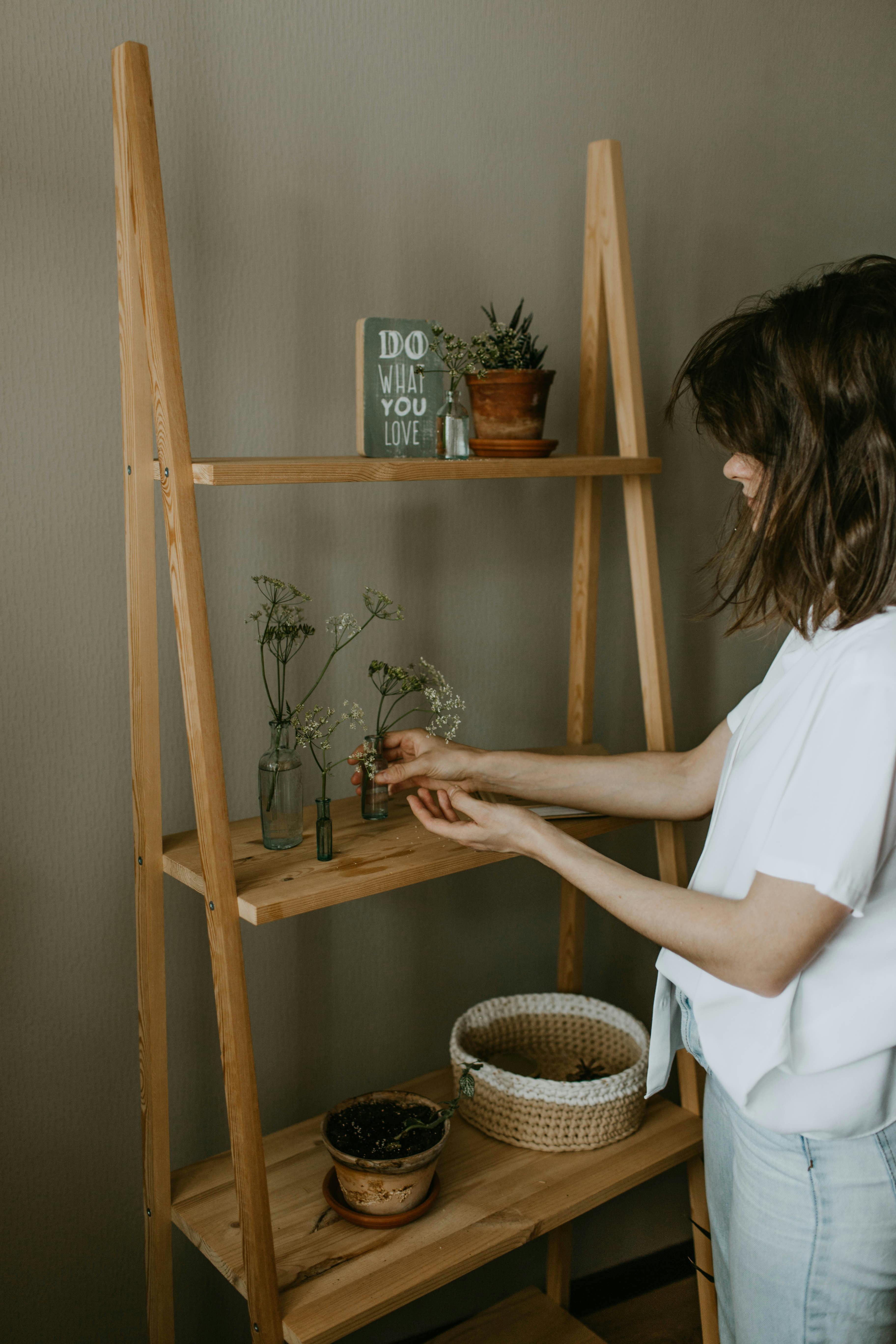 Woman organizing plants on wooden shelves in a cozy interior setting.