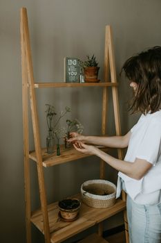 Woman organizing plants on wooden shelves in a cozy interior setting.