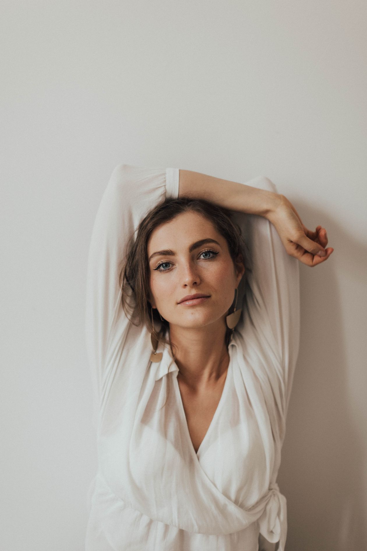 Woman in a white wrap-front blouse with long sleeves against a white wall