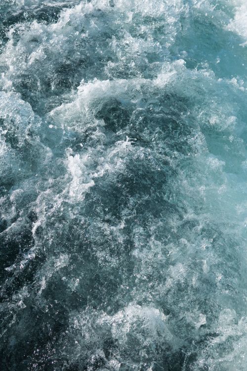 Free Abstract close-up of powerful ocean waves creating a textured pattern of white foam and blue water. Stock Photo