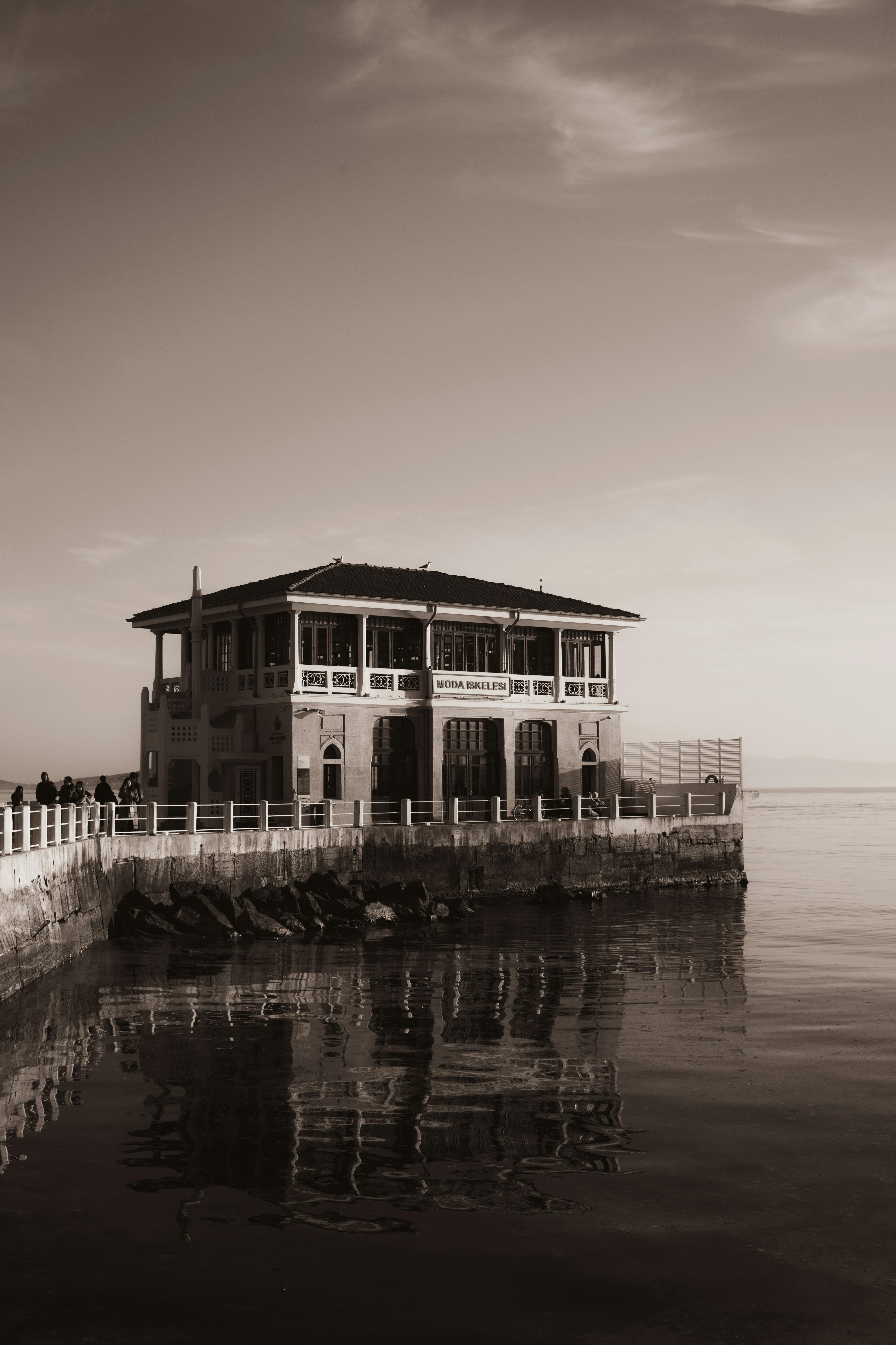 bezplatná Sépiový obrázek budovy na nábřeží odrážející se na klidné vodě na pobřeží. Základová fotografie