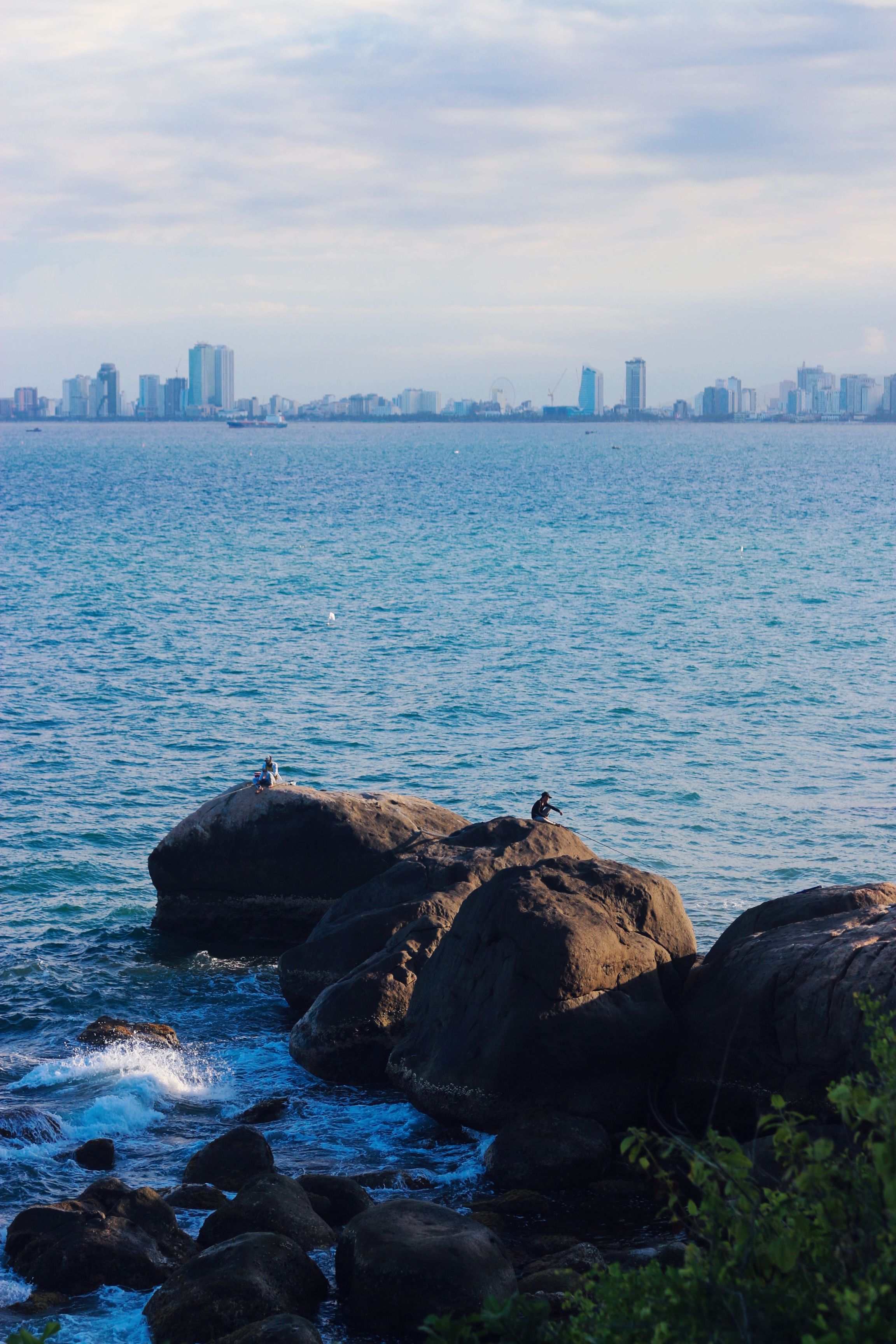 A beautiful coastal scene featuring rocky shores and the skyline of Đà Nẵng, Vietnam.