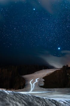 A serene winter night view of a snowy ski slope under a starry sky, perfect for stargazing.