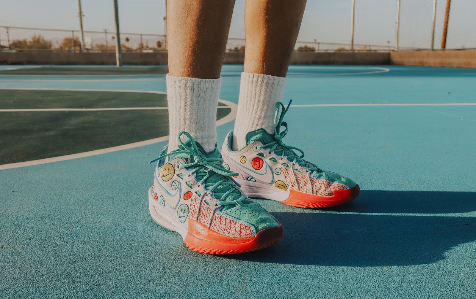 Tênis esportivos coloridos sobre o piso de uma quadra de basquete iluminada pelo sol