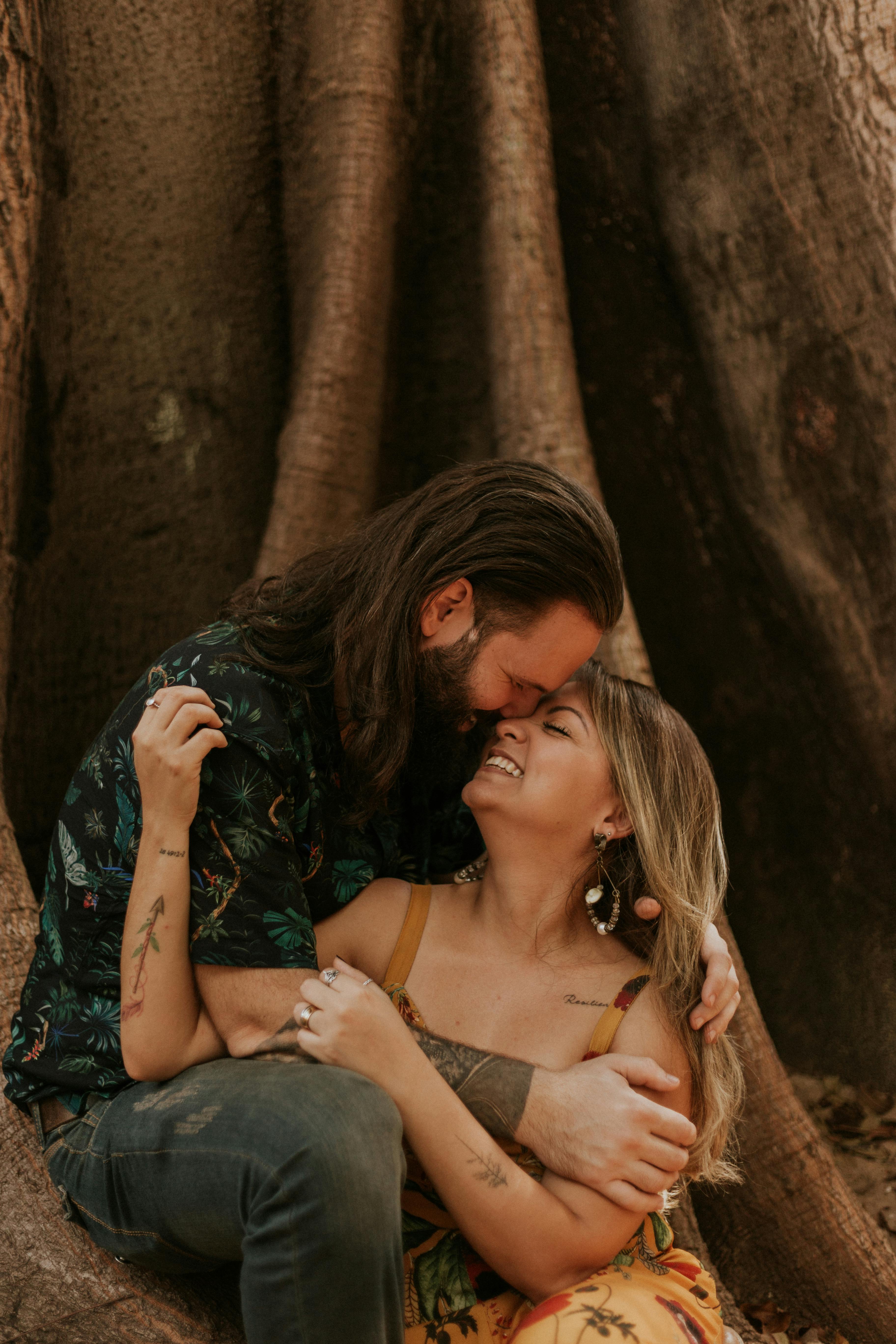 A happy couple shares an intimate moment under a large tree.