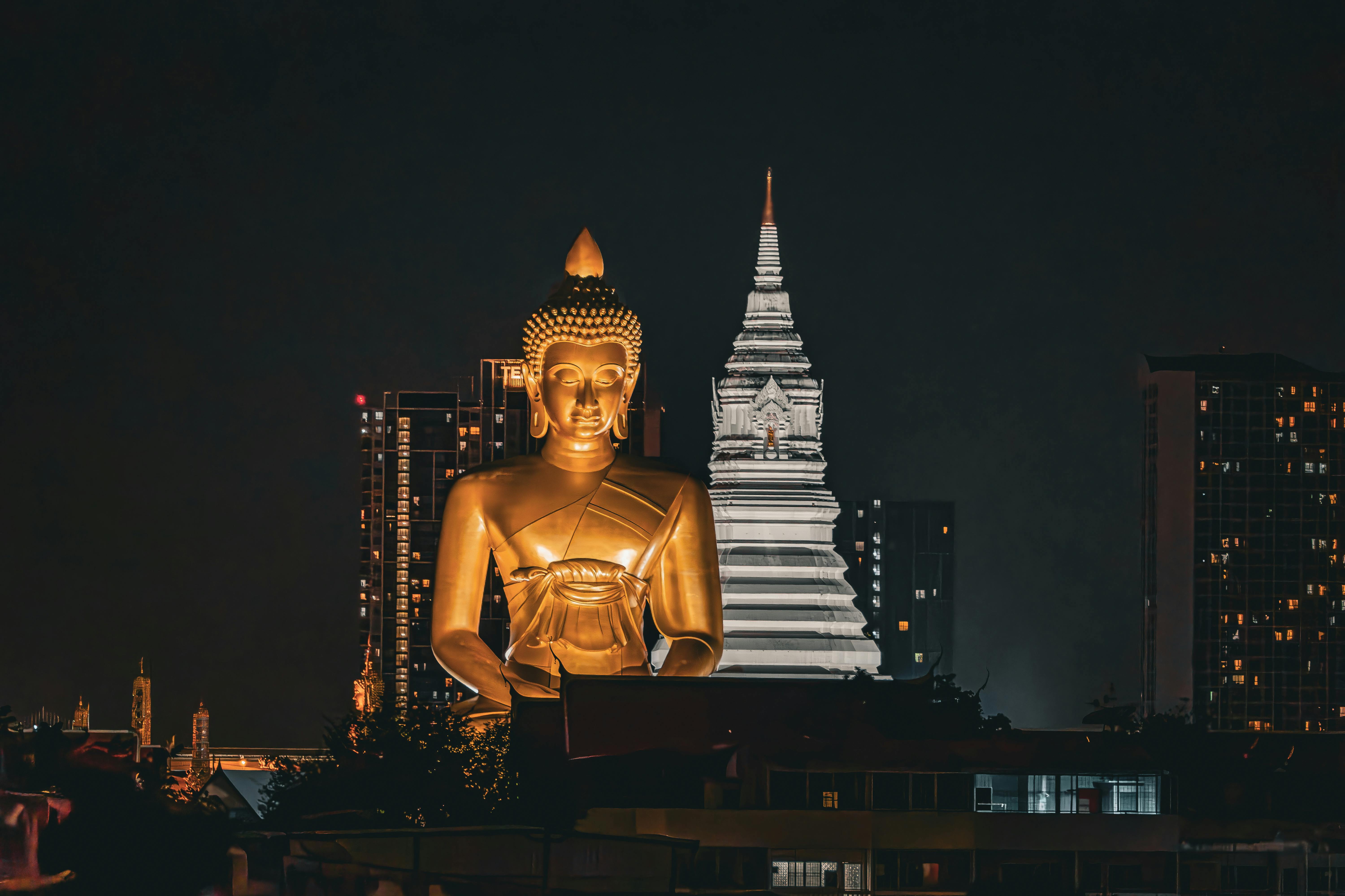 Majestic Buddha statue illuminated against Bangkok's vibrant night skyline.