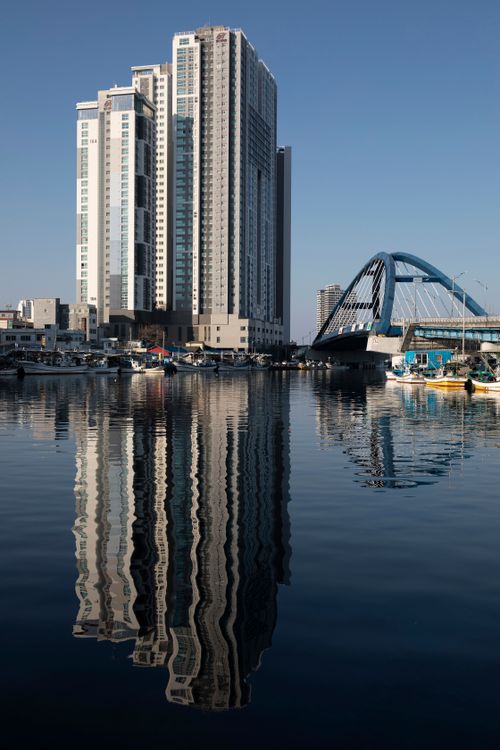 Free High-rise buildings and a bridge reflecting in a peaceful river under a clear sky. Stock Photo