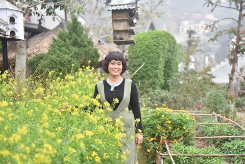 Free A woman smiling amidst yellow flowers in a lush garden on a misty day. Stock Photo