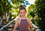 一个开朗的十几岁女孩在阳光明媚、郁郁葱葱的花园人行道上微笑