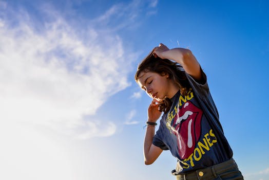 一个十几岁的女孩在晴朗的天空下举起双臂，享受着阳光明媚的一天，散发着青春与自由的气息