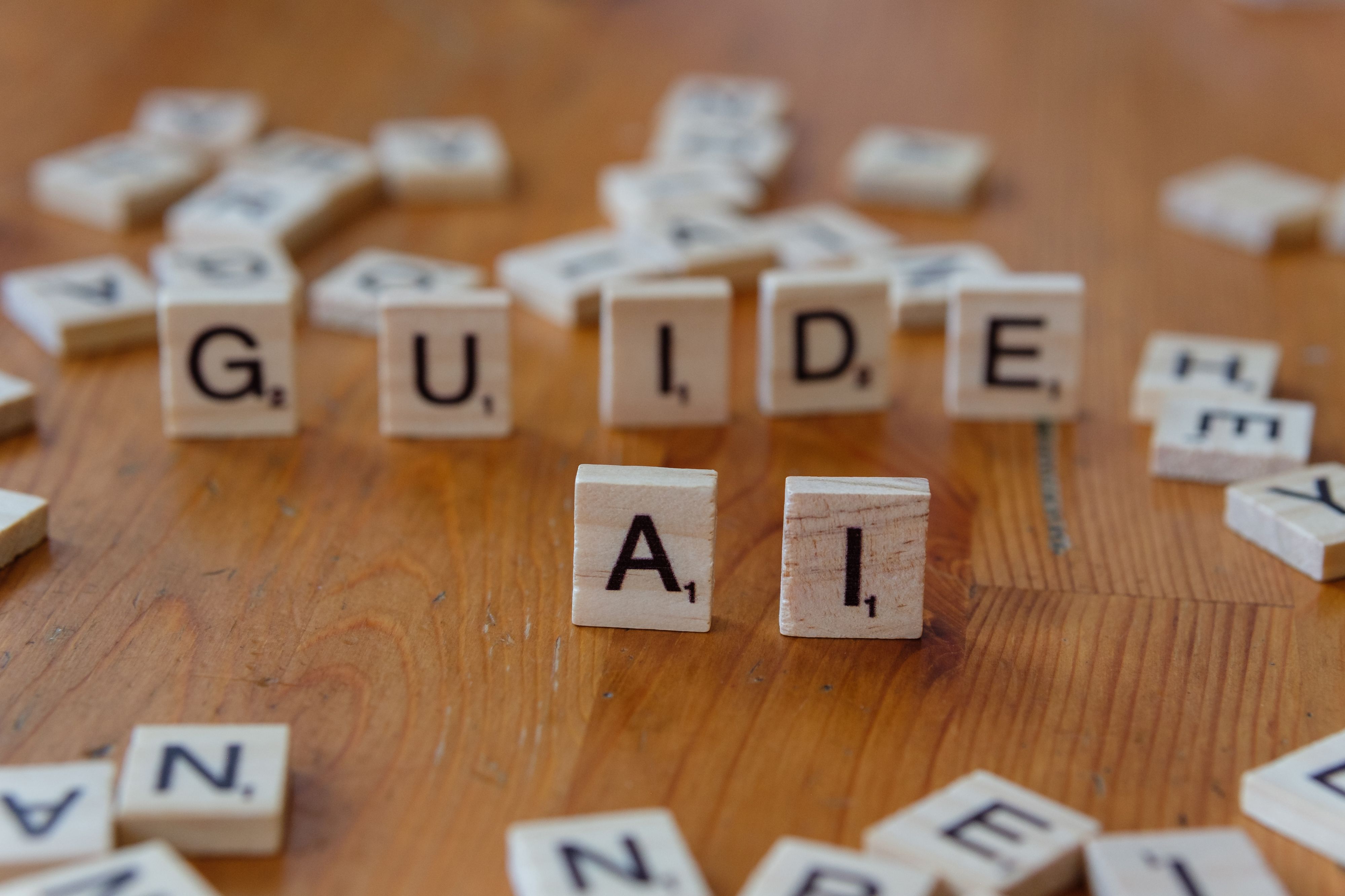 Gratis Letras de Scrabble que deletrean 'GUIDE' y 'AI' sobre una superficie de madera, lo que sugiere dirección y tecnología. Foto de stock