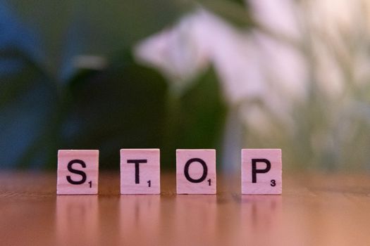 Close-up of Scrabble tiles spelling STOP on wooden table.