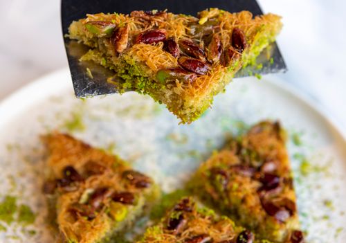 Free Close-up of a pistachio and almond baklava slice on a spatula, showcasing its texture. Stock Photo