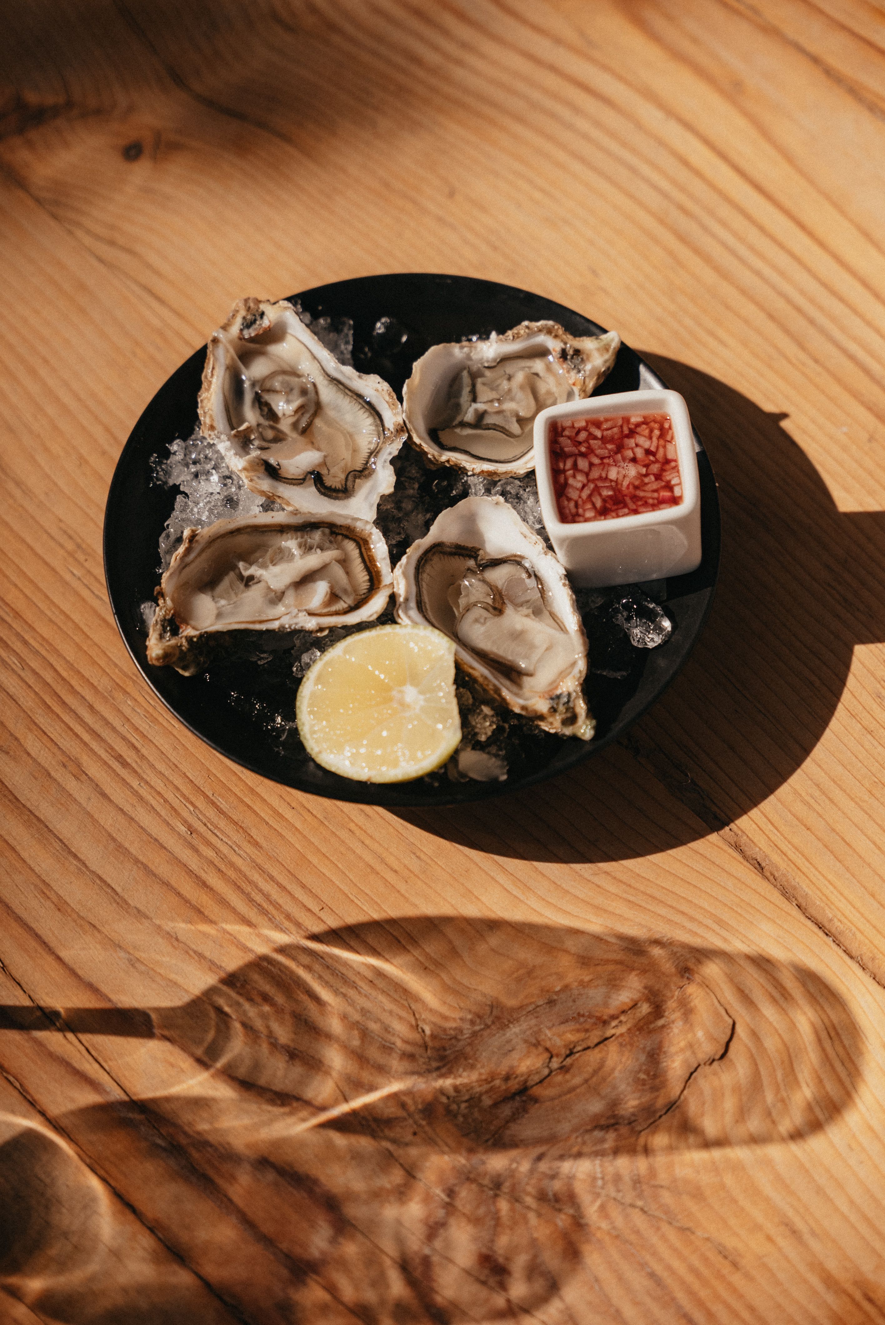 A delicious serving of oysters on ice with lemon and sauce on a wooden table.