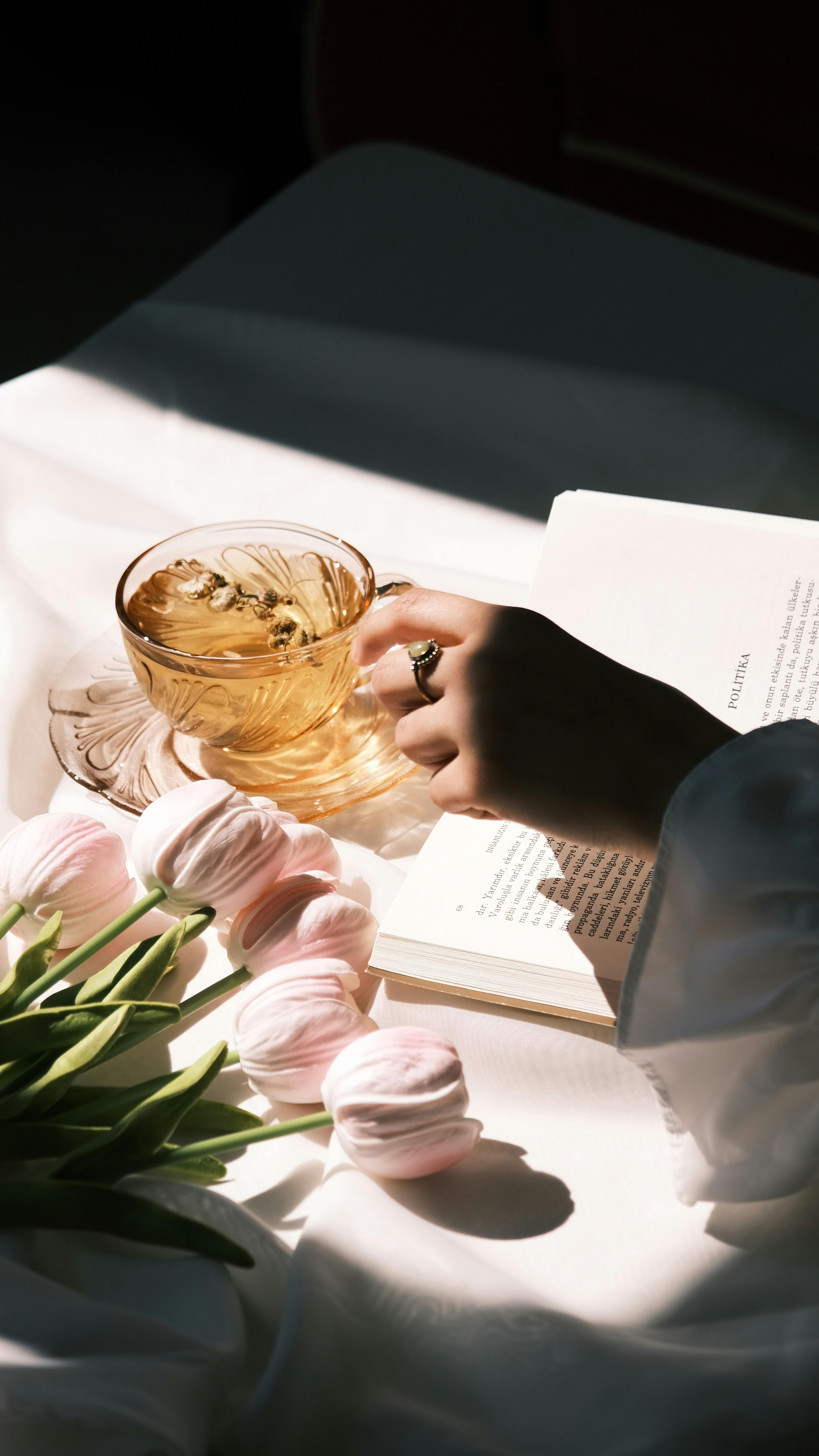 A serene moment with tea, tulips, and a book in natural light.