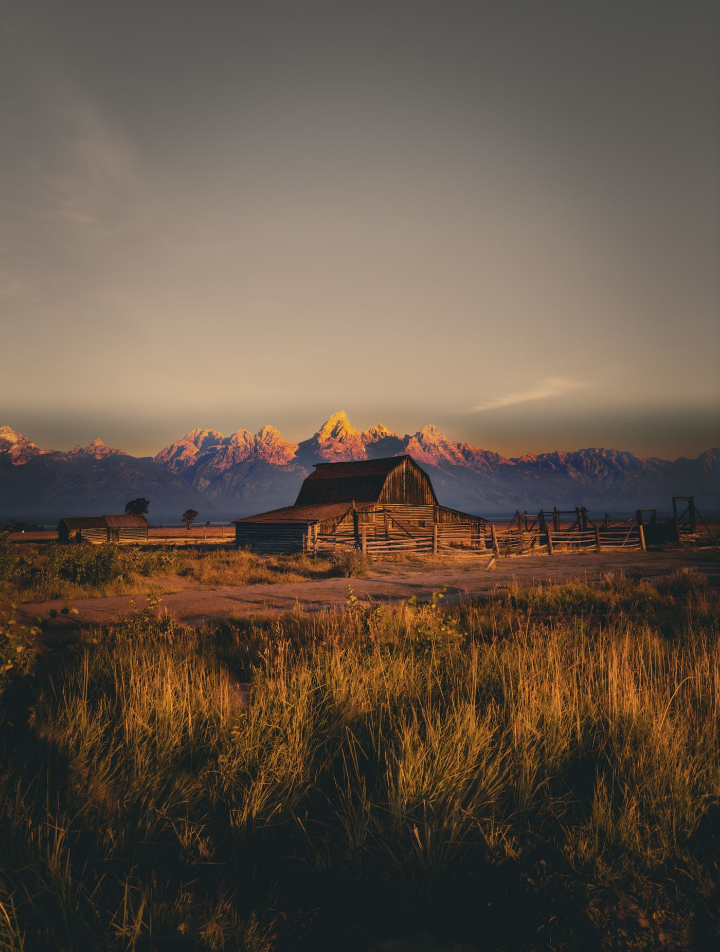 A rustic barn in Wyoming against a mountain backdrop at sunset