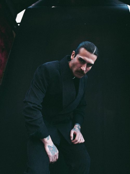 Free Dramatic portrait of a tattooed man in dark attire against a moody background. Stock Photo