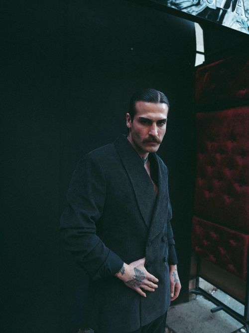 Free A man with tattoos in a dark suit poses in a dimly lit setting. Stock Photo