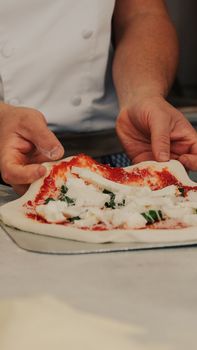 Professional chef preparing fresh pizza with tomato sauce and basil in an Italian kitchen.