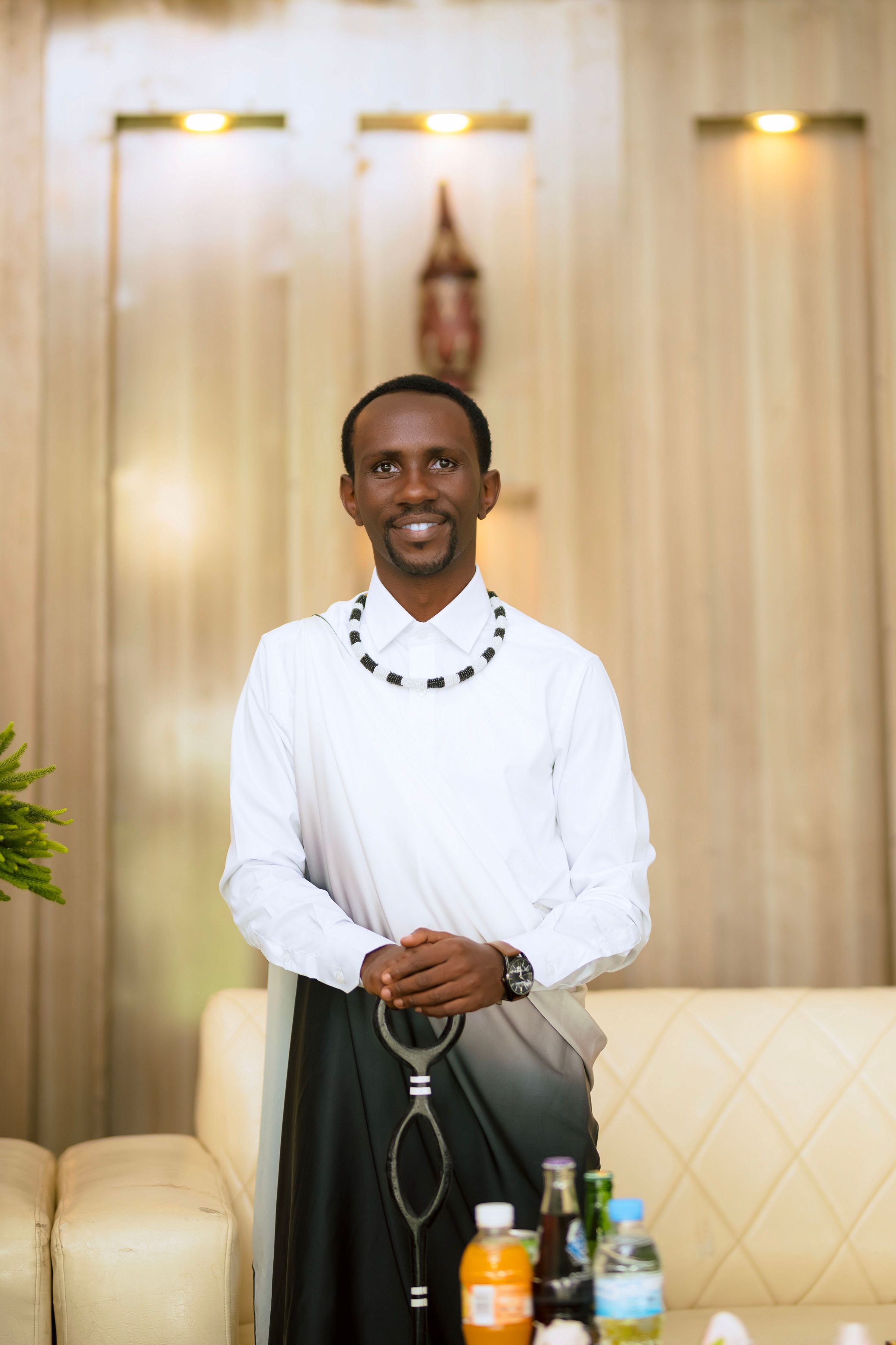 Smiling man in traditional African attire standing with beverages on a table.