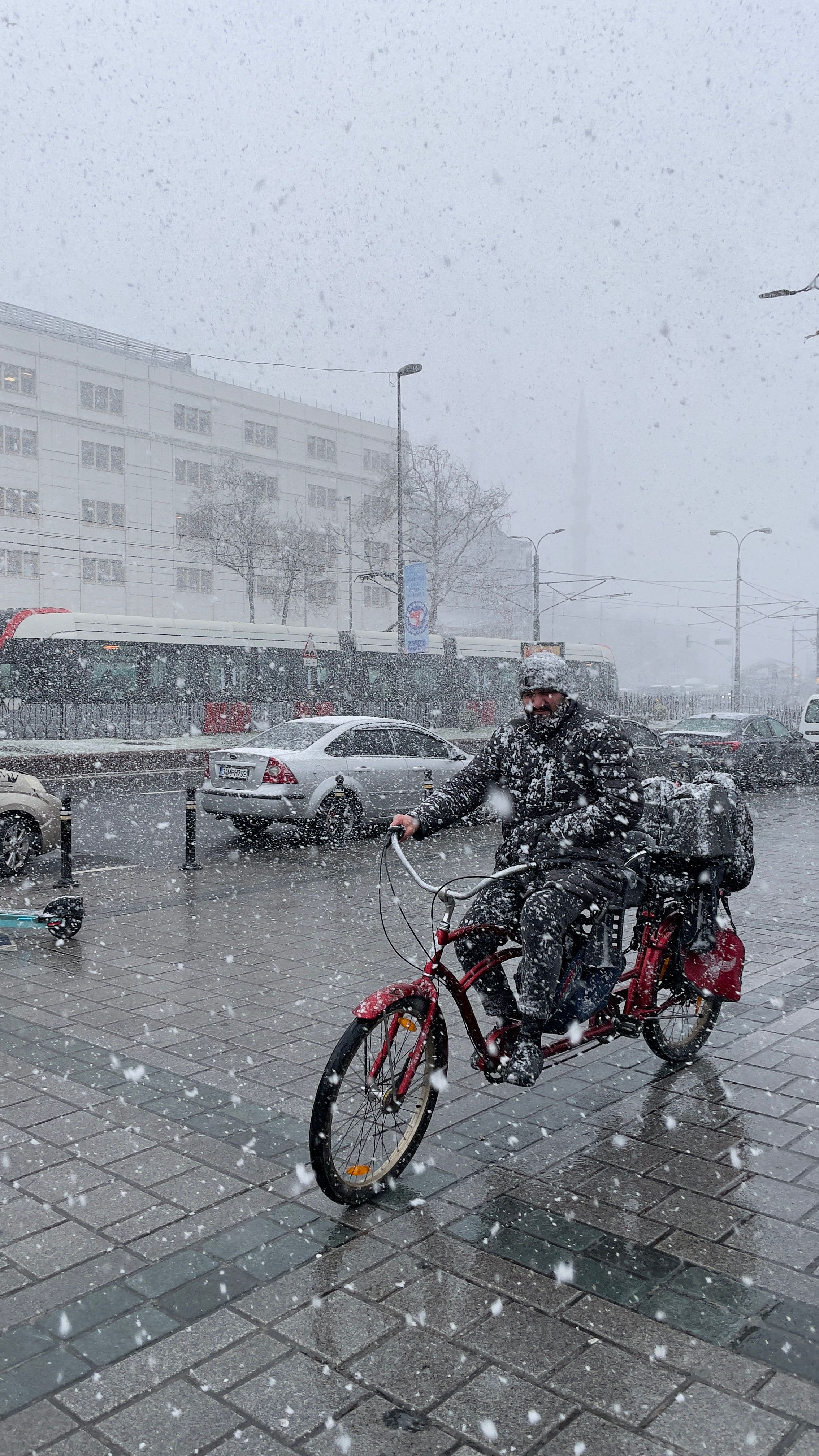 A cyclist navigates the snow-covered urban streets during a heavy snowfall, showcasing winter resilience.