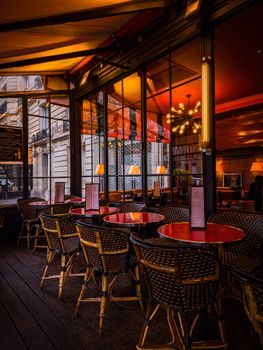Cozy Paris café interior with wicker chairs and red tables in warm lighting.