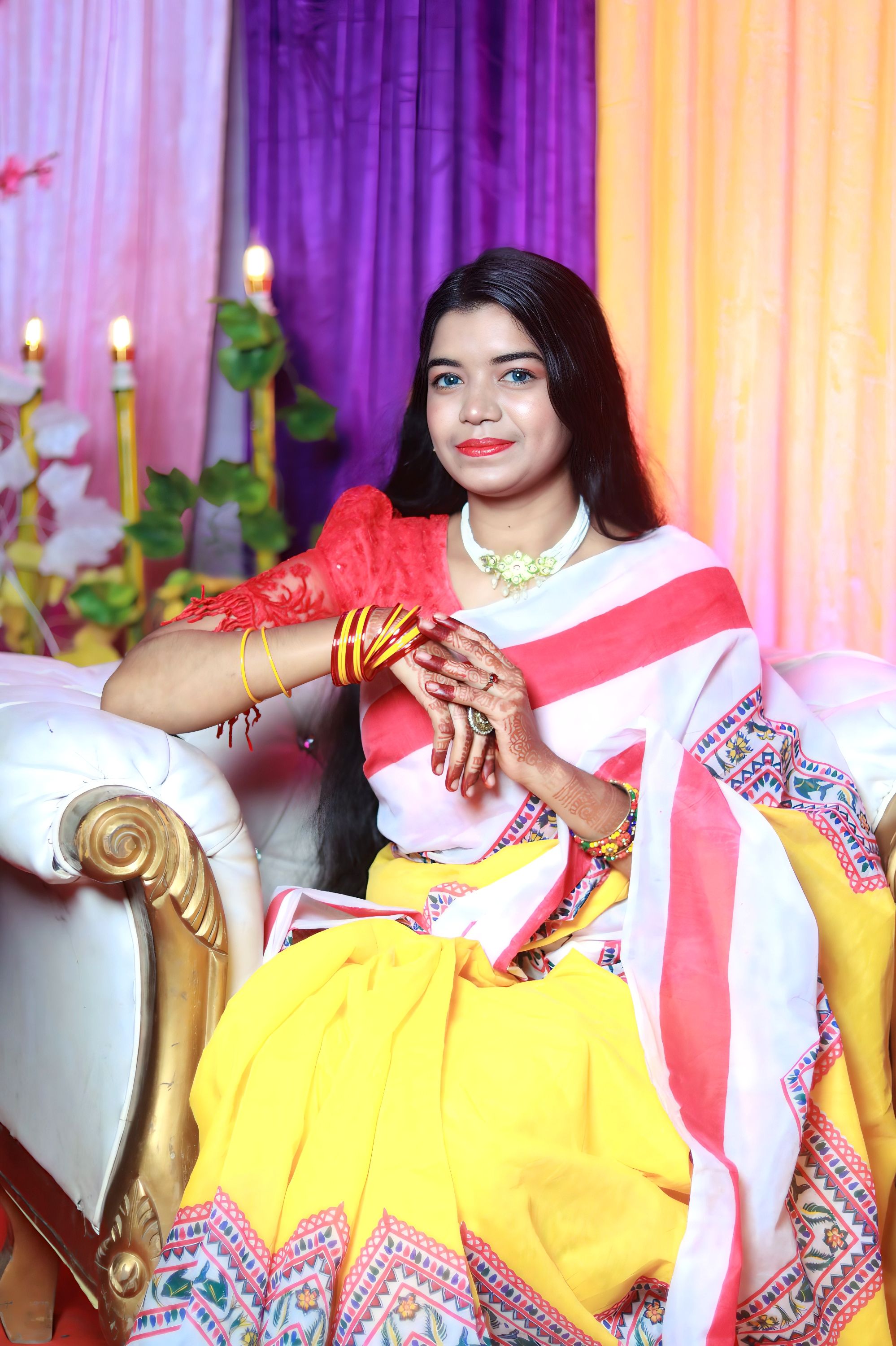 Smiling woman in colorful saree sitting on ornate couch. Vibrant setting.