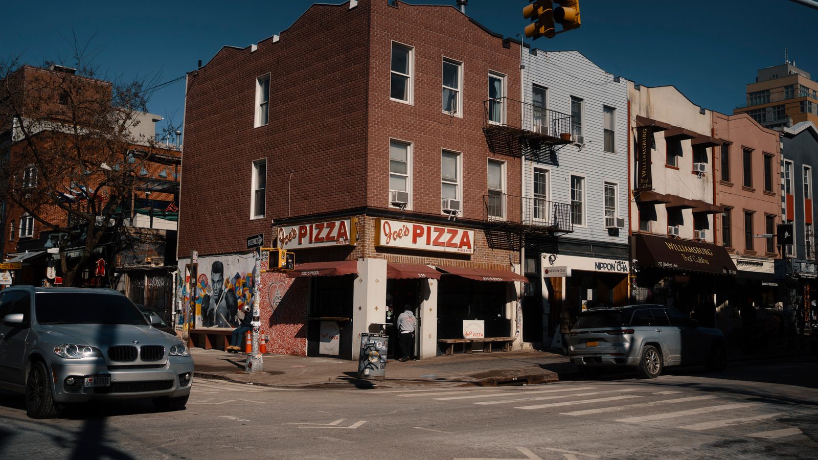 Street view of Joe's Pizza on a sunny day in Brooklyn, showcasing the lively urban atmosphere.