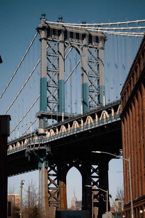 Free View of Manhattan Bridge with Empire State Building framed underneath, clear day in NYC. Stock Photo