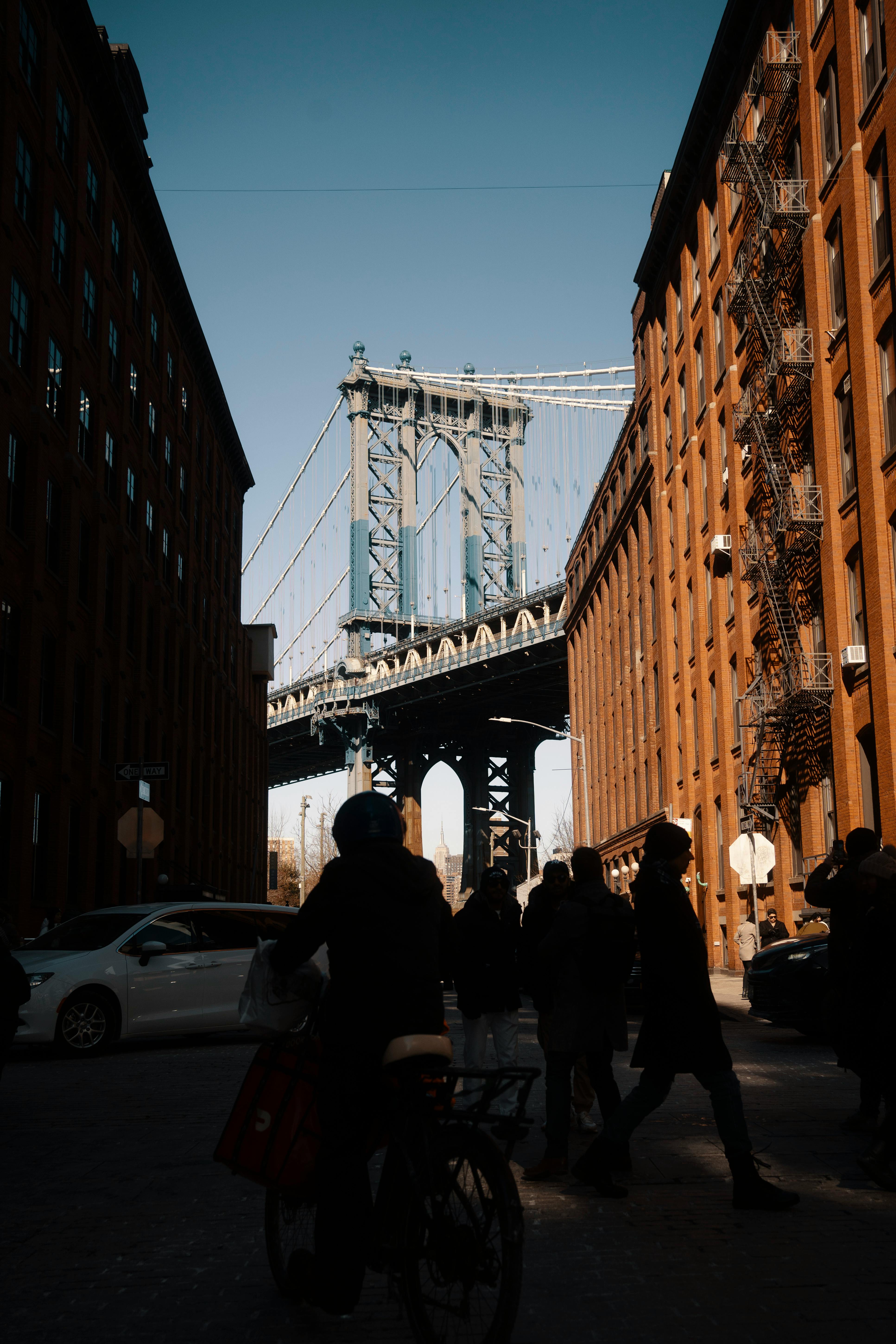 Silhouetted pedestrians and cyclist against Manhattan Bridge in New York City.