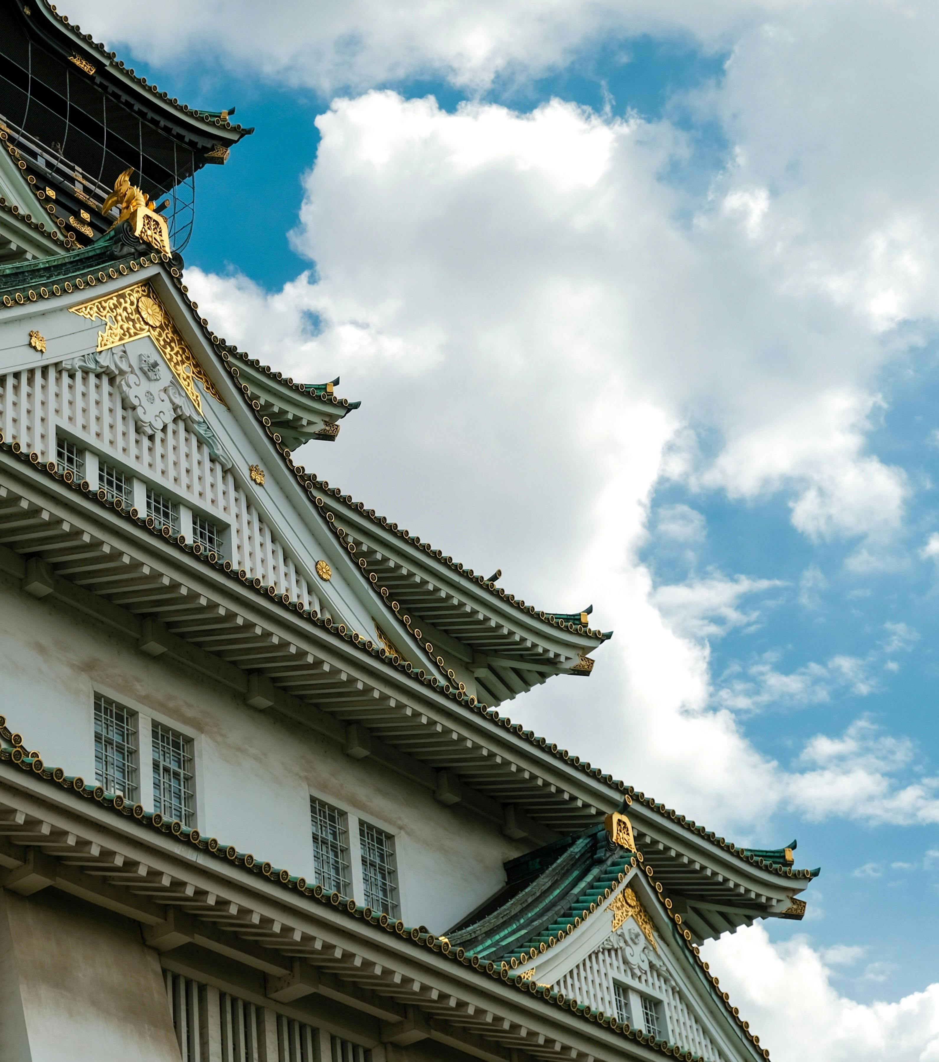 View of Osaka Castle's ornate rooftop against a bright blue sky with clouds.
