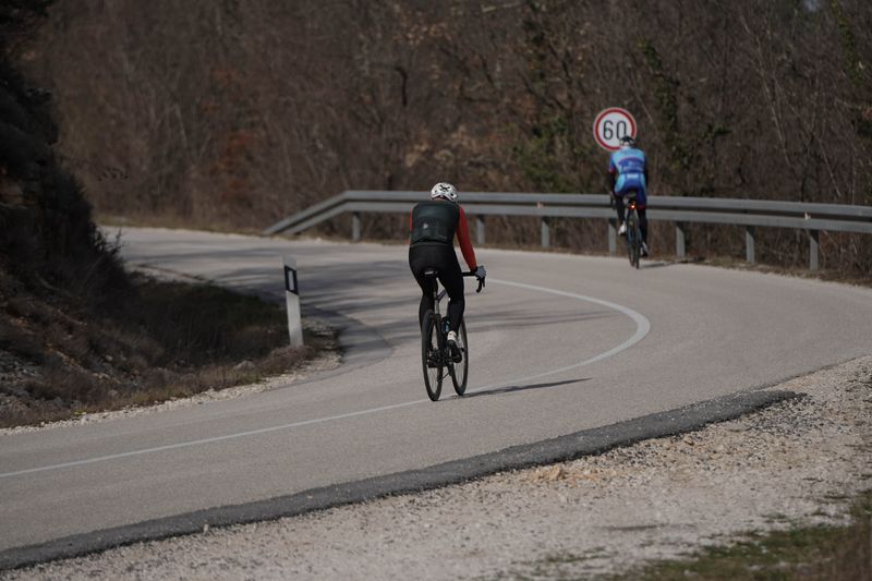 Two cyclists ride uphill on a winding road in Croatia with a speed limit sign in view.