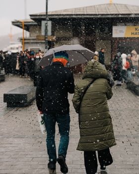 Two people walking under an umbrella on a snowy day in a city setting.