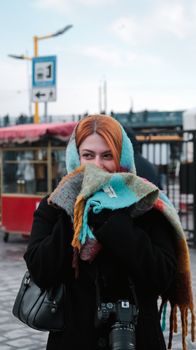 Woman with orange hair smiling in winter, wrapped in a colorful scarf, outdoors.
