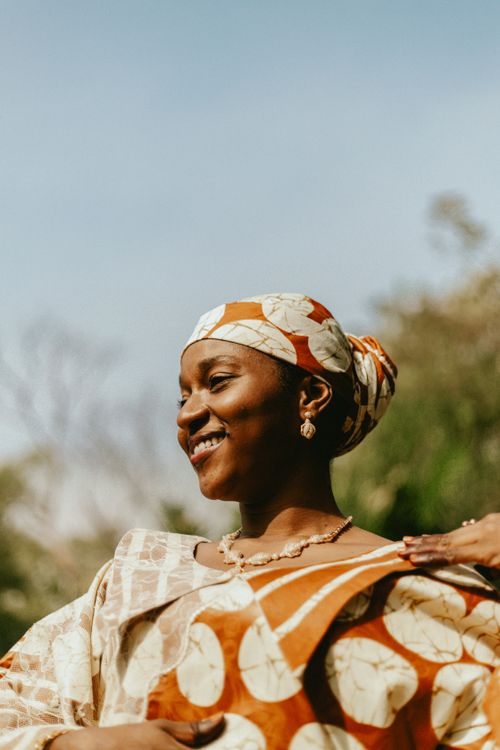 Free A joyful woman wearing traditional African clothing smiles in a sunny outdoor setting. Stock Photo