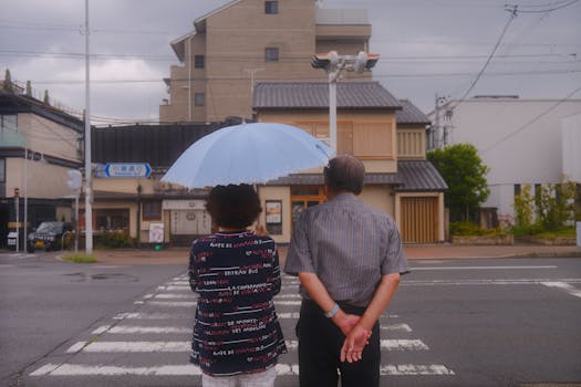 A couple stands at a crosswalk in Kyoto, Japan, under an umbrella on a cloudy day.