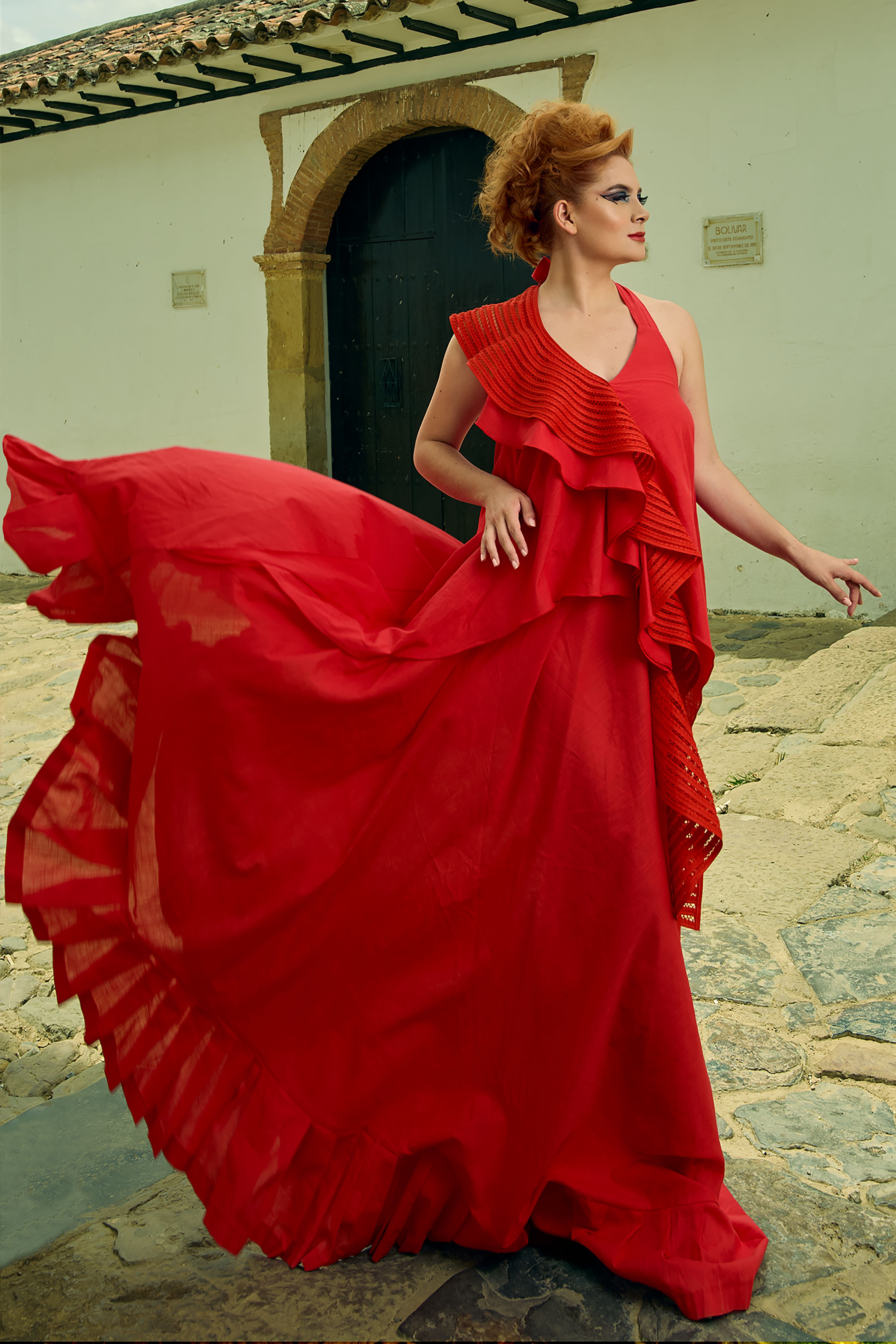 Stunning woman in a red dress poses stylishly in historic Villa de Leyva, Colombia.
