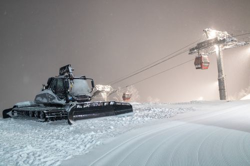 Free A snowcat working under night lights on a snowy ski slope, with cable cars in the background. Stock Photo