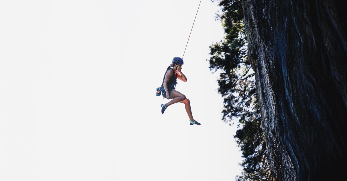 A woman rappels down a cliff with safety gear on a clear day. Adventure and exploration.