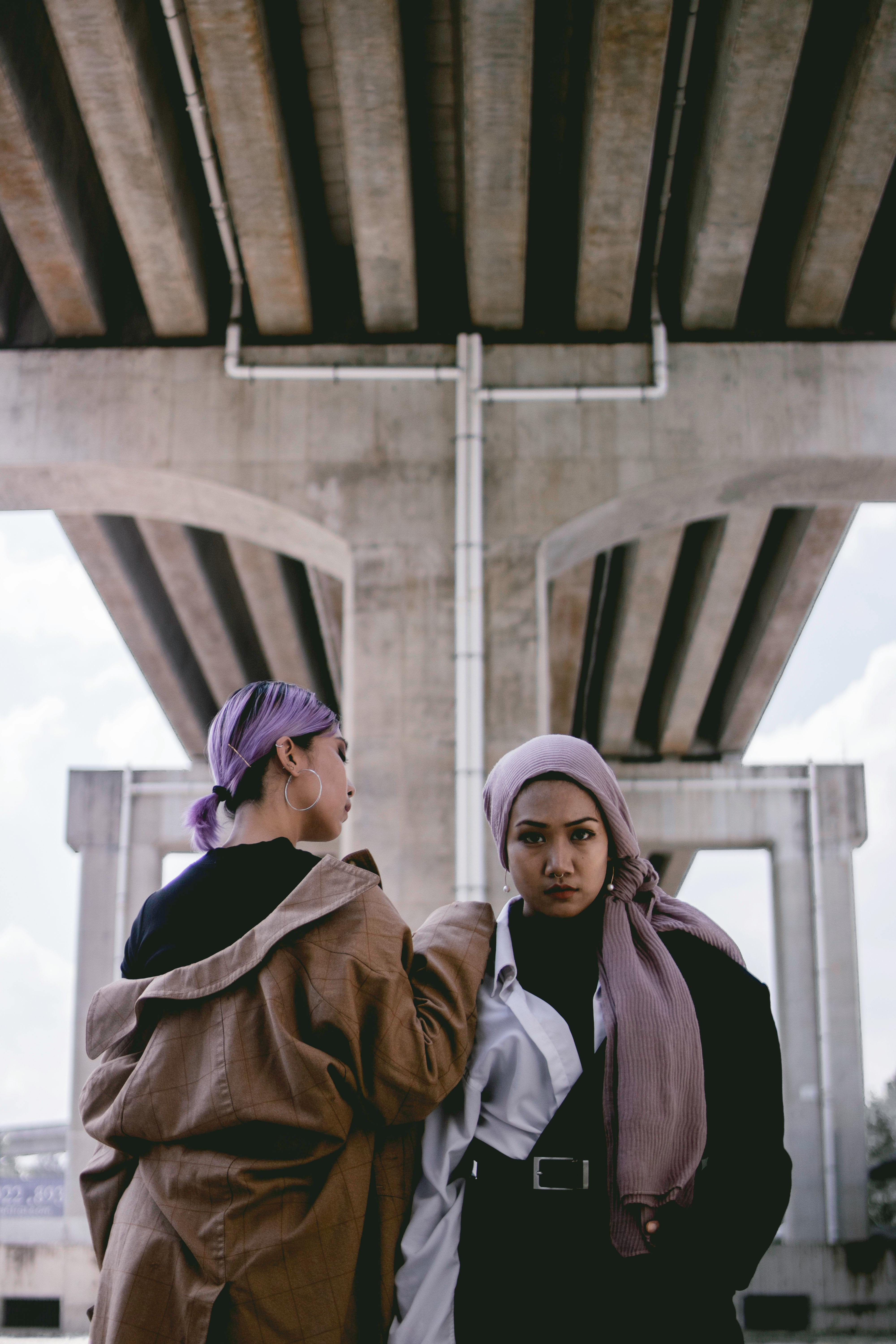 两名时尚女性自信地在现代城市桥下摆姿势，展现当代街头风格