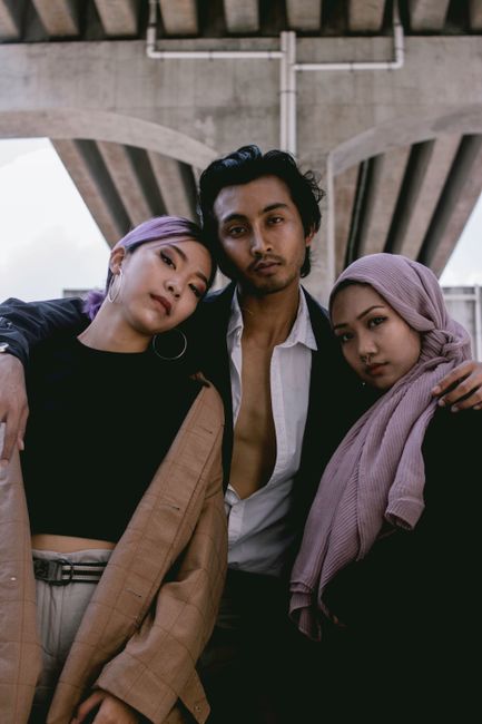 Three fashionable individuals posing confidently under an urban bridge setting.