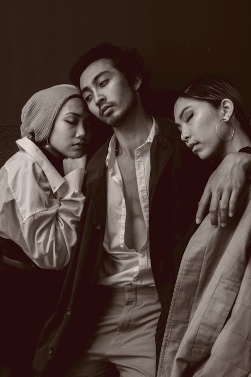 Black and white Asian guy in trendy clothes embracing ethnic women with closed eyes