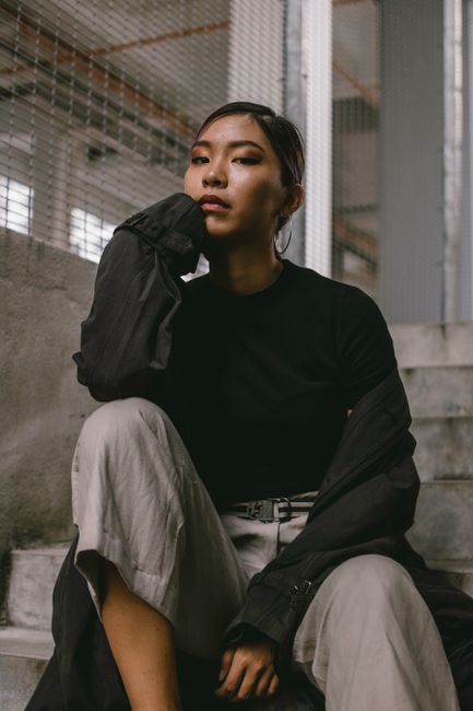 A thoughtful woman sitting on concrete stairs in an industrial setting, exuding a stylish and introspective vibe.