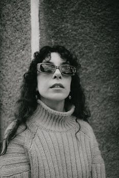 Stylish black and white portrait of a woman wearing sunglasses and a woolen sweater.