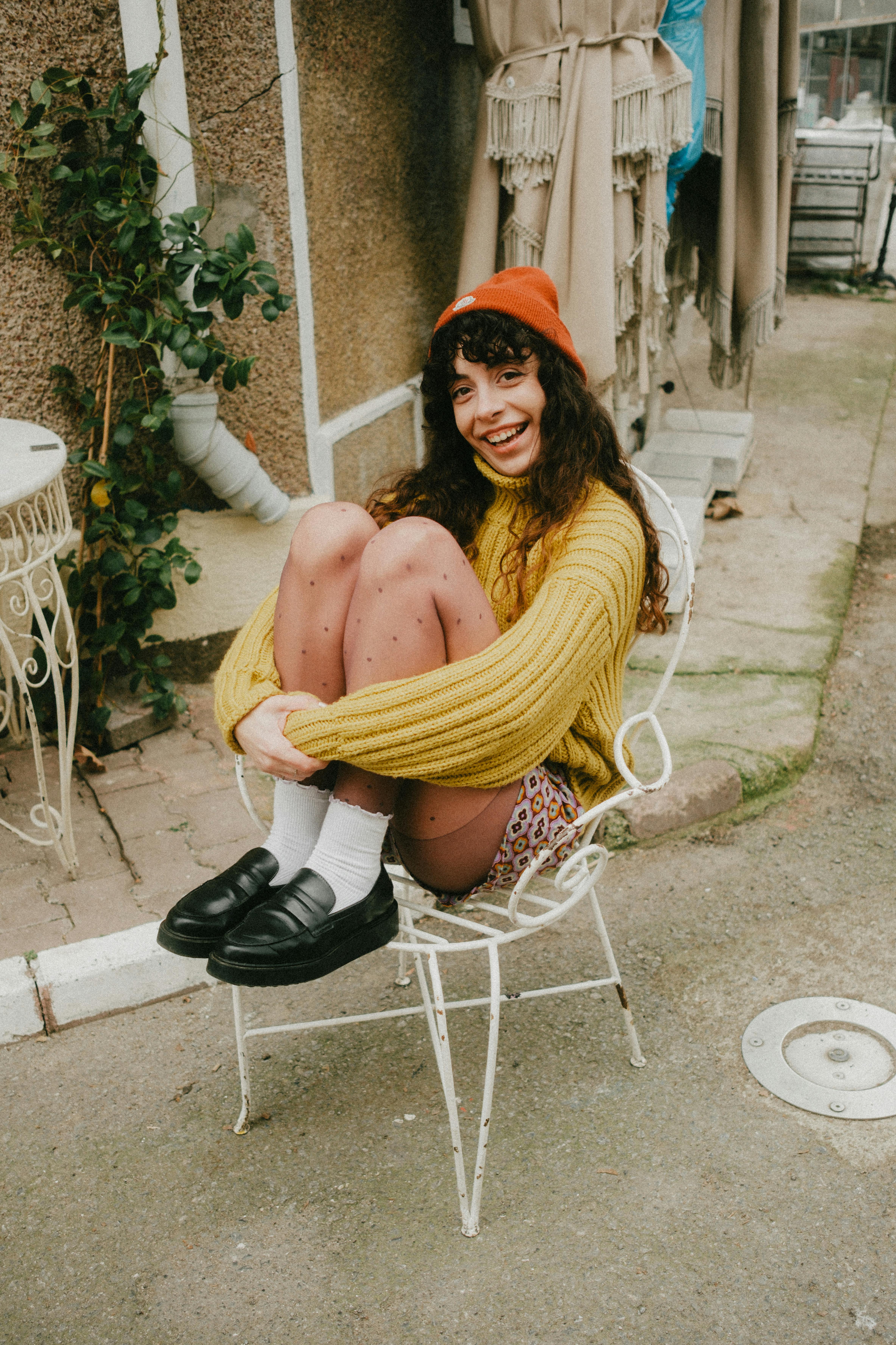 Cheerful young woman sitting outside in autumn attire, embracing the cozy fall vibes.