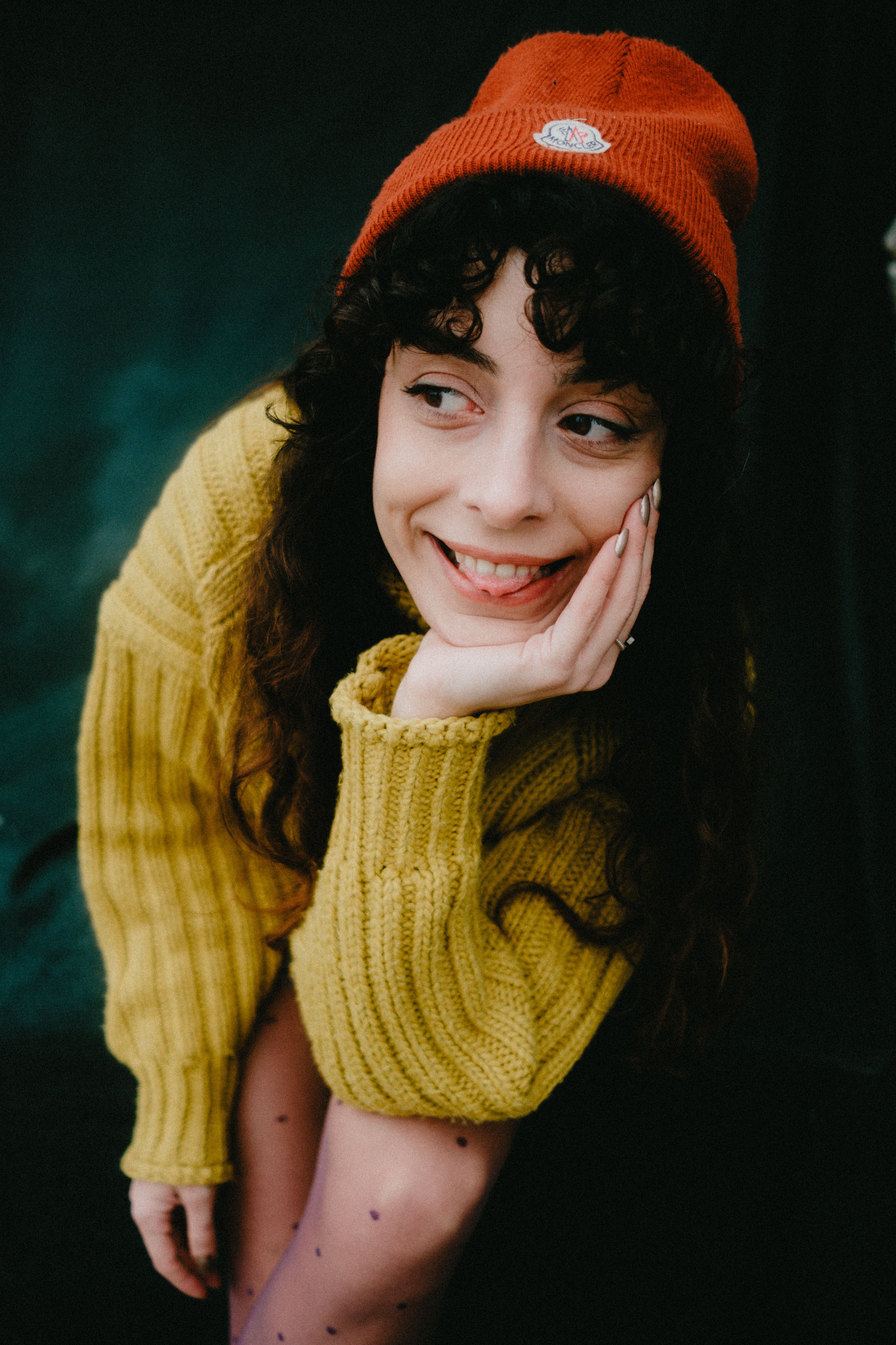 Young woman in a cozy yellow sweater and red beanie smiling warmly outdoors.