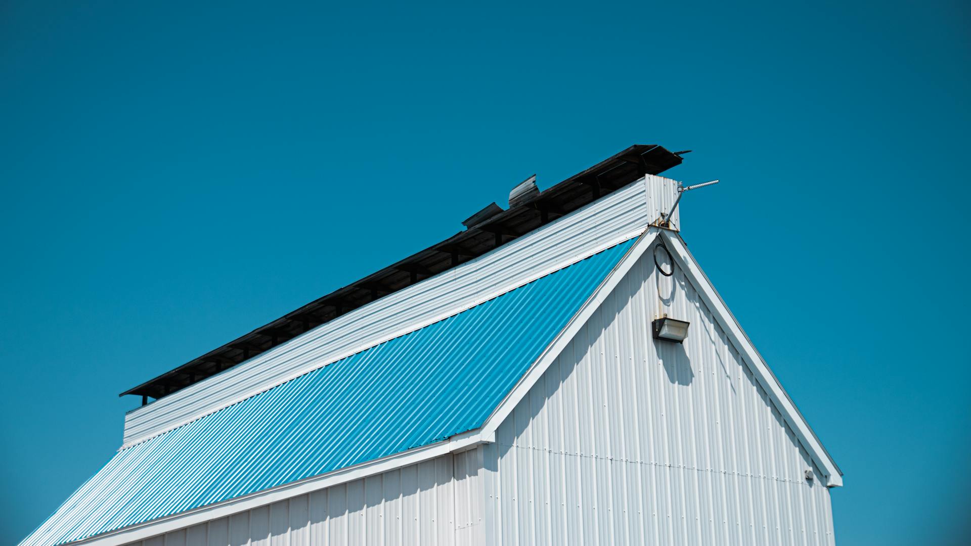 A white barn with a blue metal roof under a bright clear sky in Montreal.